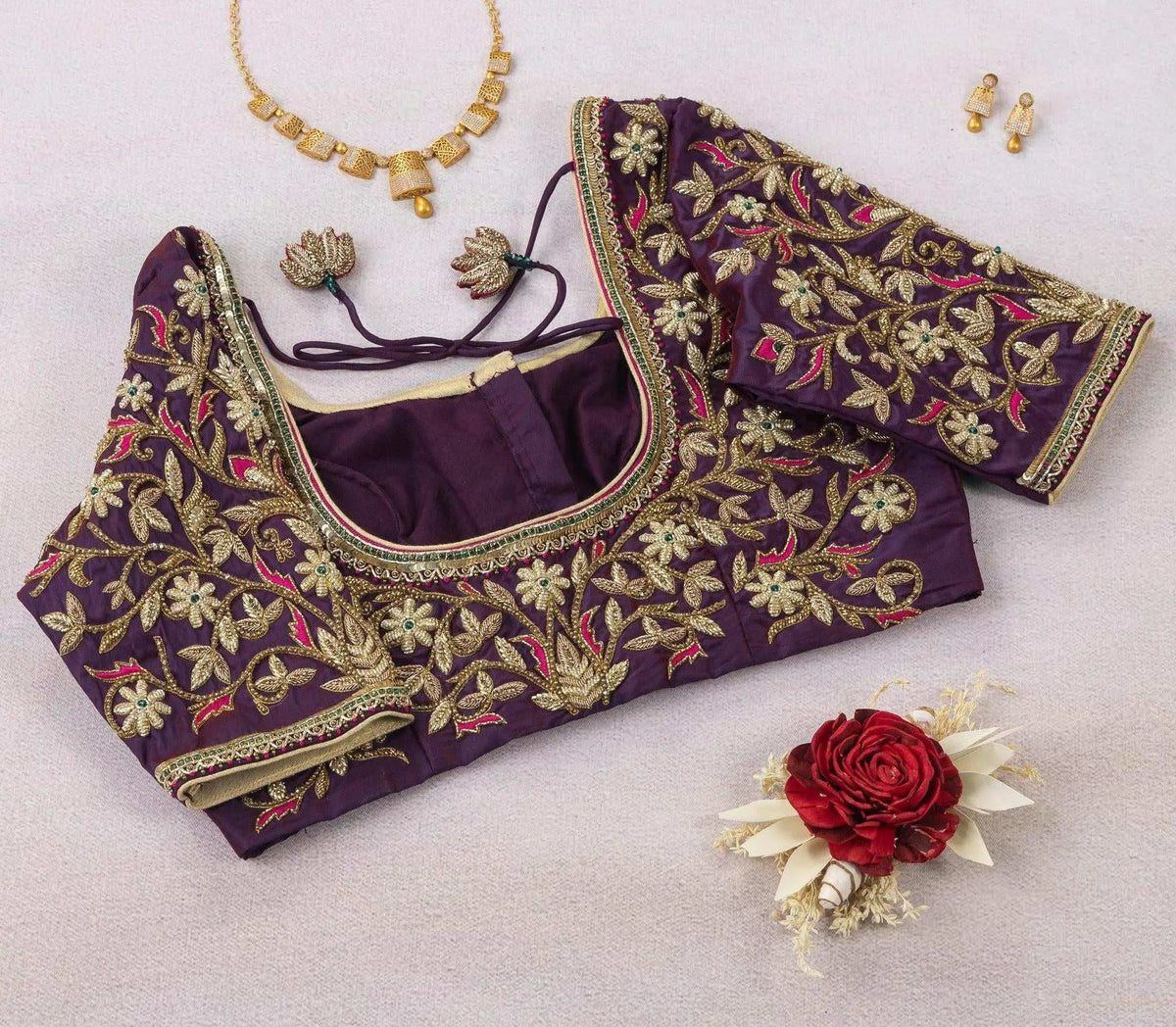 Back of the purple embroidered blouse laid flat, styled with a gold necklace and a red rose