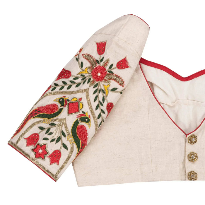Sleeve close-up with green parrots, red blooms and gold zari on ivory fabric
