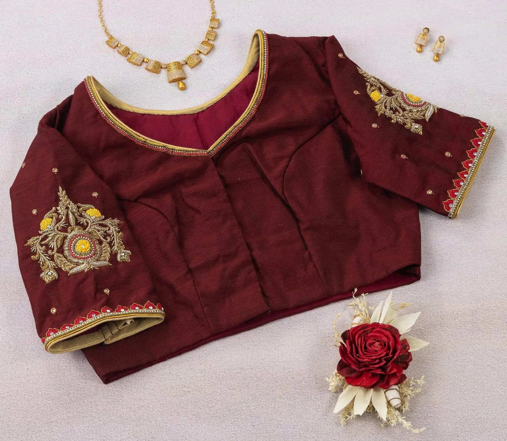 Maroon blouse laid with a sleeve folded over, plain V-neck panel and gold piping in view