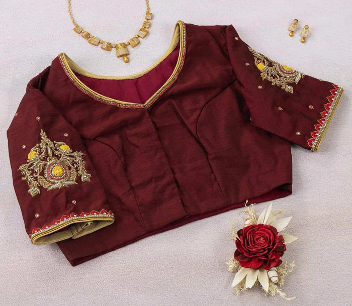 Maroon blouse laid with a sleeve folded over, plain V-neck panel and gold piping in view