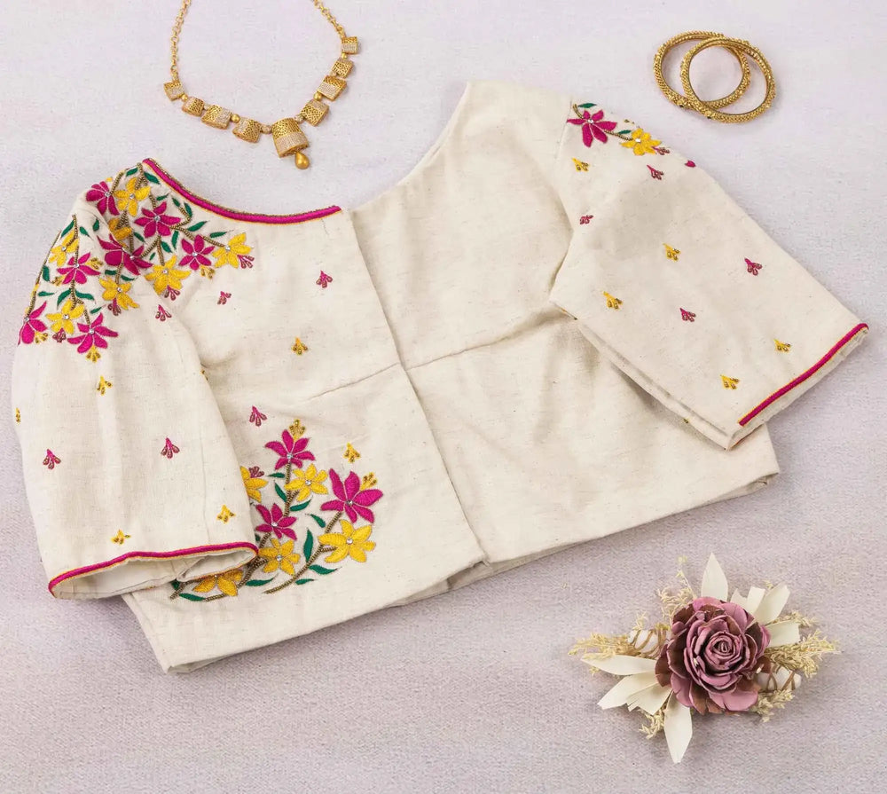 Ivory floral blouse laid out with sleeves spread, gold necklace and bangles alongside