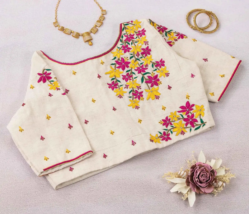 Off-white blouse folded flat, pink and yellow floral embroidery spilling from the neckline