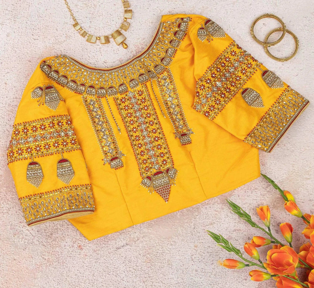 Yellow jhumka blouse flat-laid back up, embroidered yoke beside a gold necklace and bangles