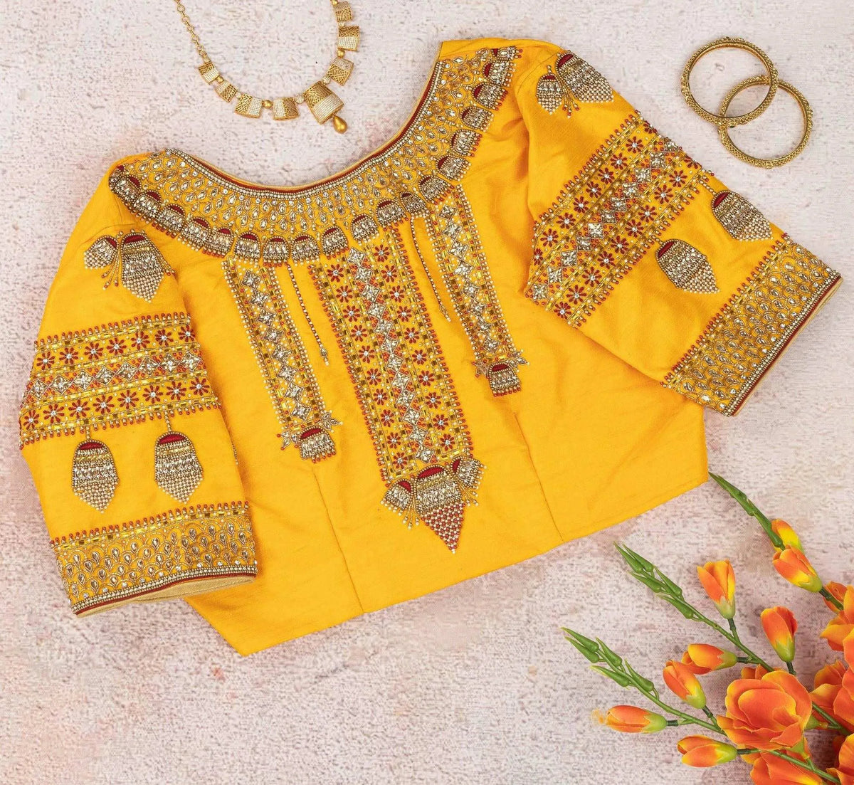 Yellow jhumka blouse flat-laid back up, embroidered yoke beside a gold necklace and bangles