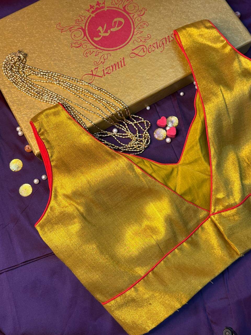 Sleeveless gold tissue blouse laid flat with a beaded gold chain and gift box