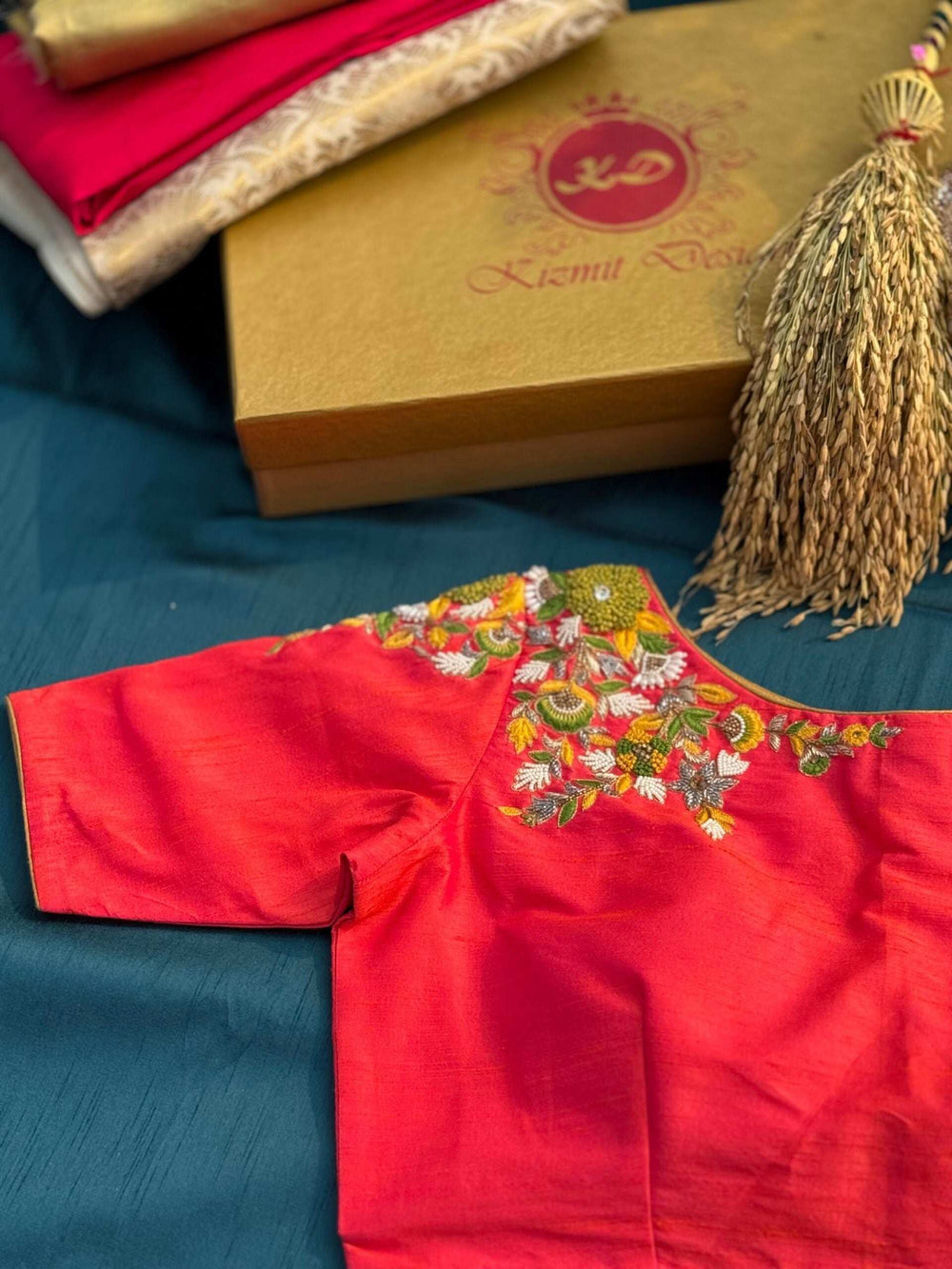 Multicoloured floral embroidery on the shoulder of the pink blouse, gift box behind