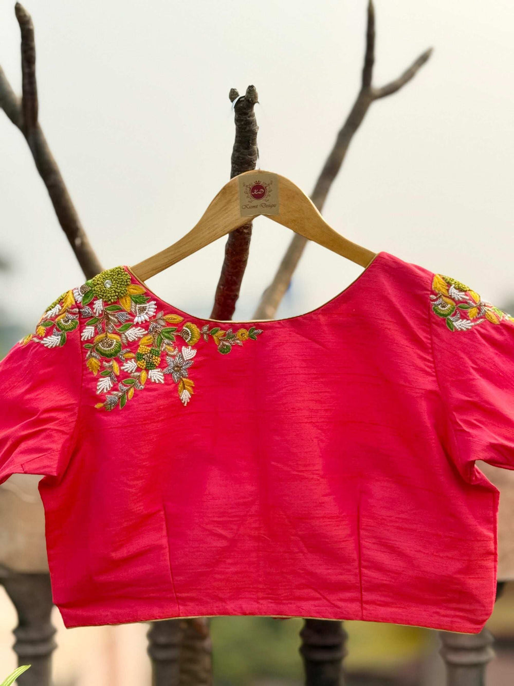 Pink blouse on a wooden hanger outdoors, wide neck with embroidered shoulders