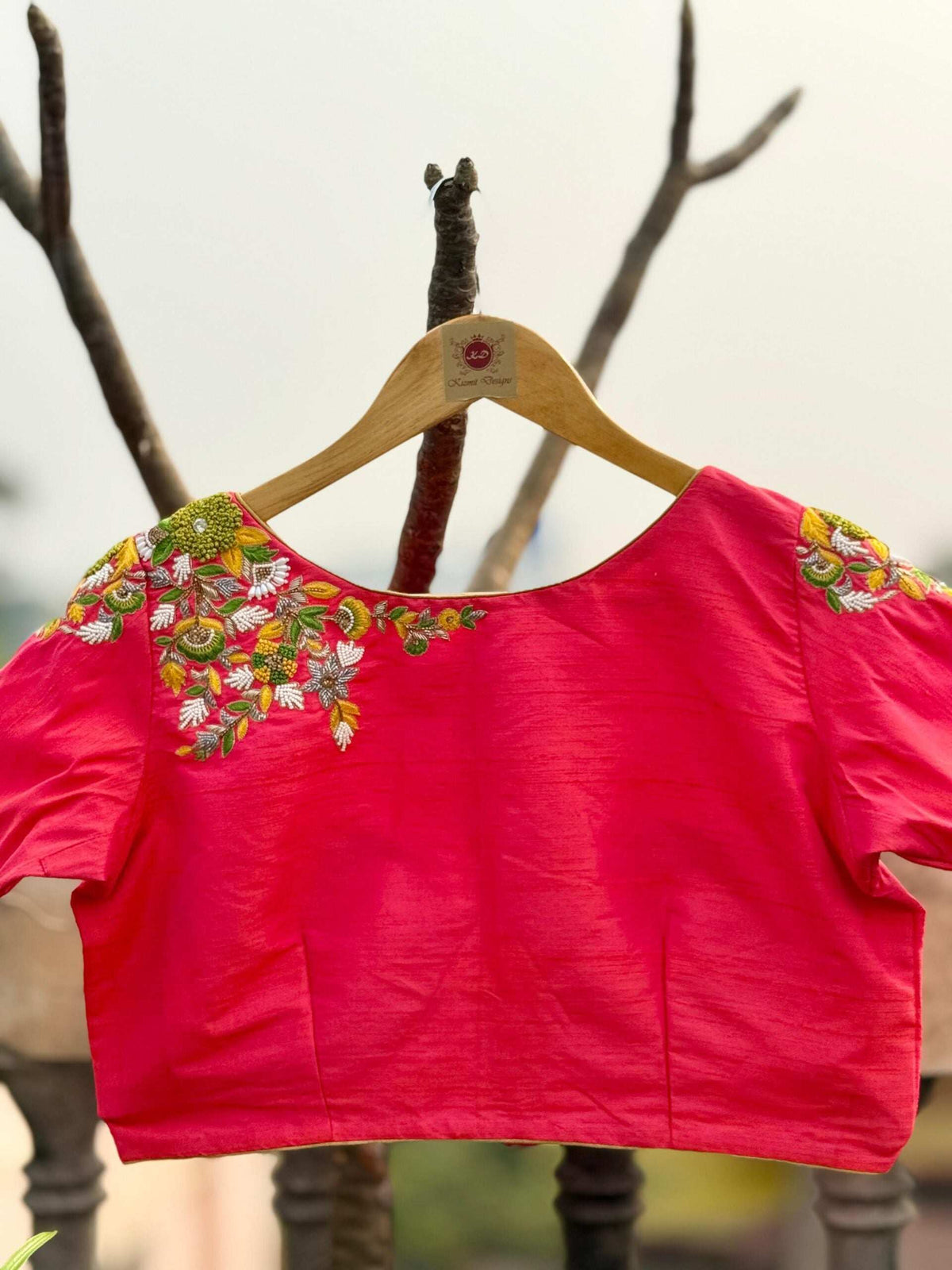 Pink blouse on a wooden hanger outdoors, wide neck with embroidered shoulders