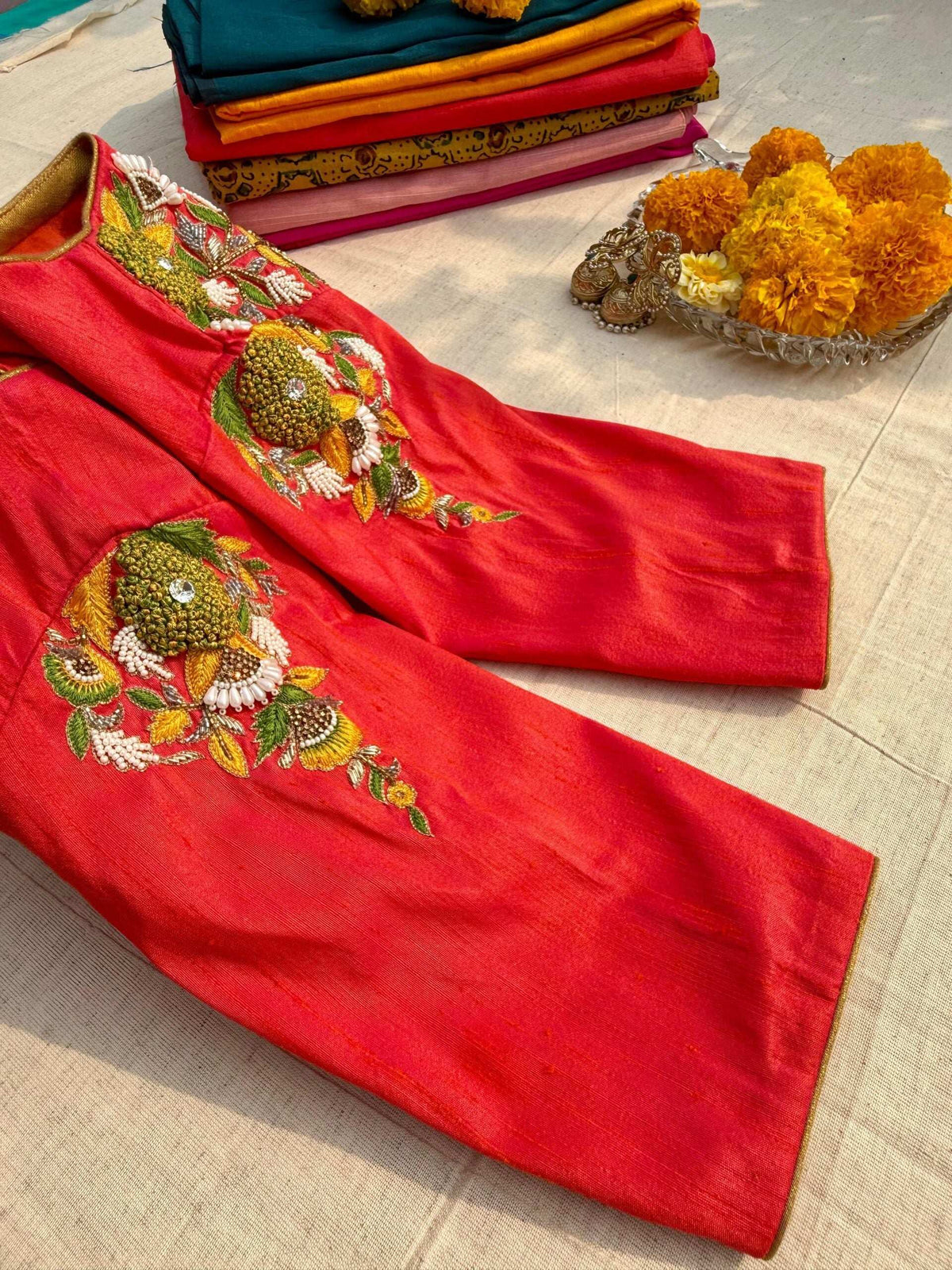 Sleeve and shoulder flowers on the folded pink blouse, marigolds and fabrics behind