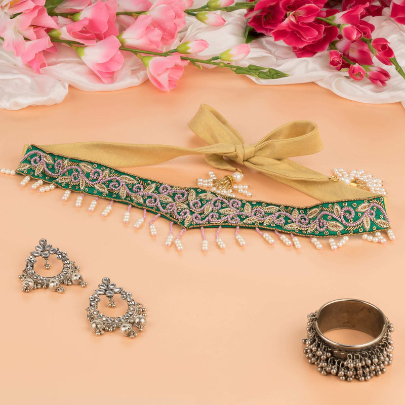 Bottle green saree belt with gold and pink embroidery and pearl drop fringe, laid out with earrings
