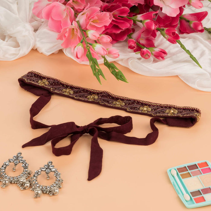 Maroon saree belt tied in a bow, styled with pink blooms and jhumka earrings