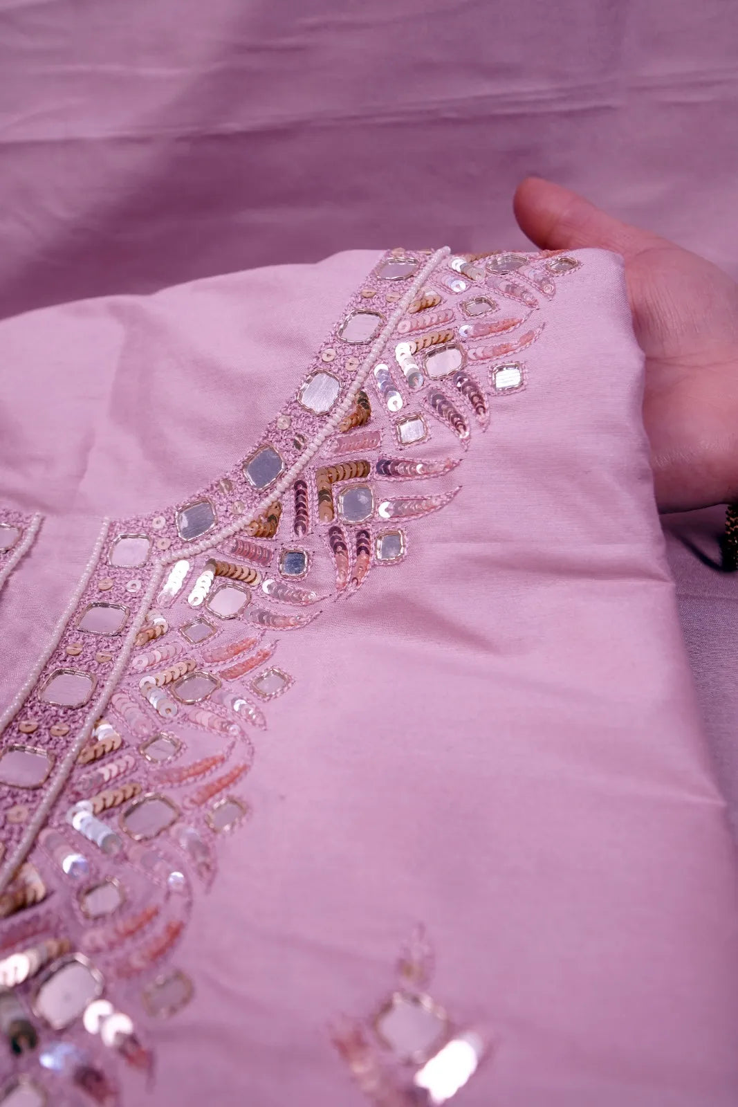 Close-up of mirror and sequin embroidery along the pink neckline, fabric held in hand