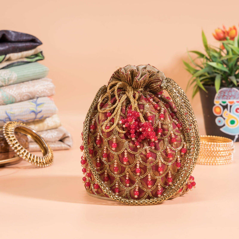 Cherry red potli bag with gold scallop beadwork, styled beside bangles and folded fabrics