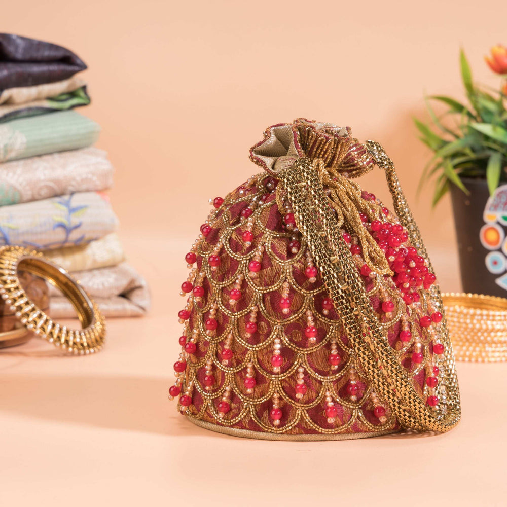 Scalloped rows of red beads and gold zari across the potli, set against stacked fabrics