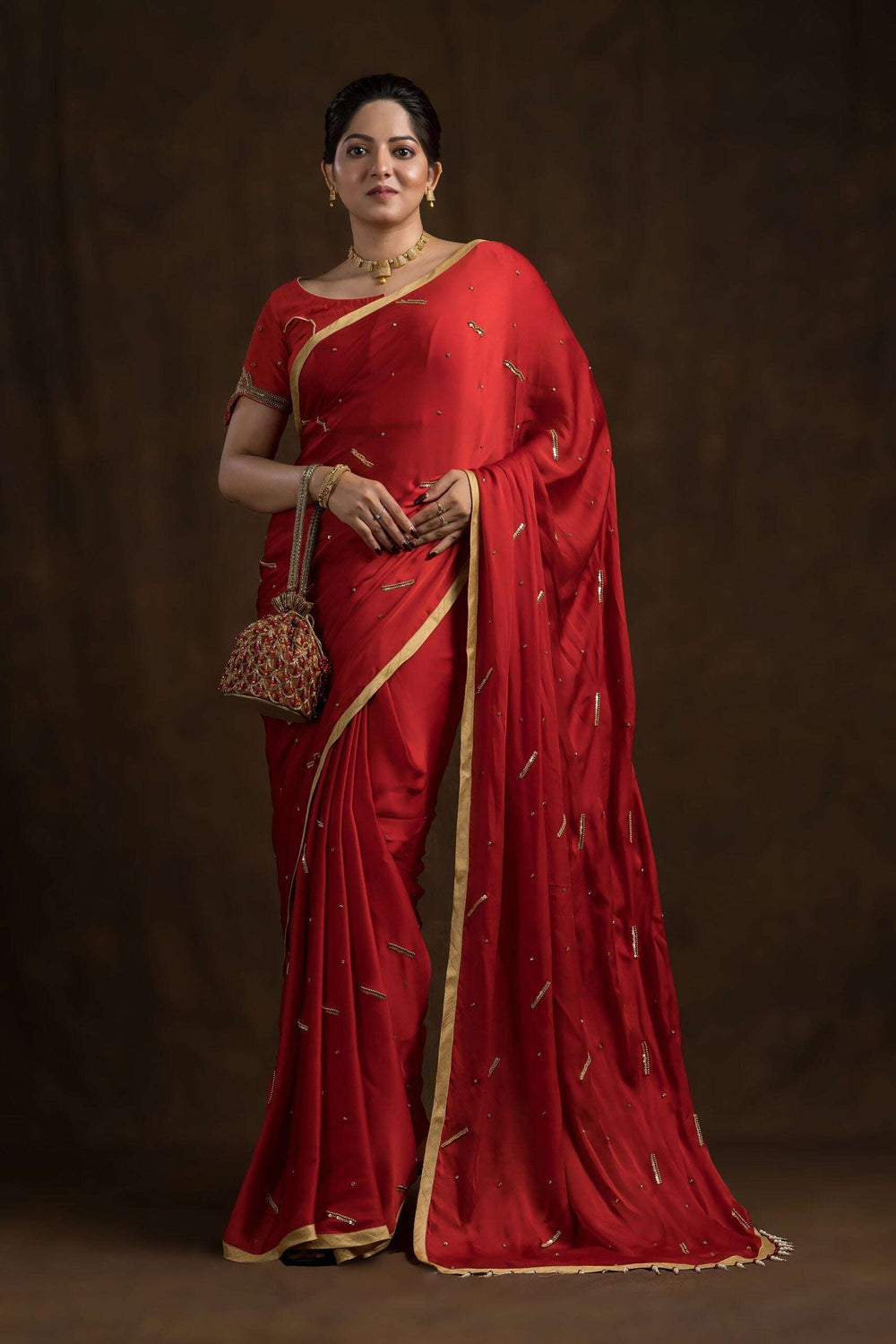 Model in a red saree holding the cherry red potli bag at her waist, full length
