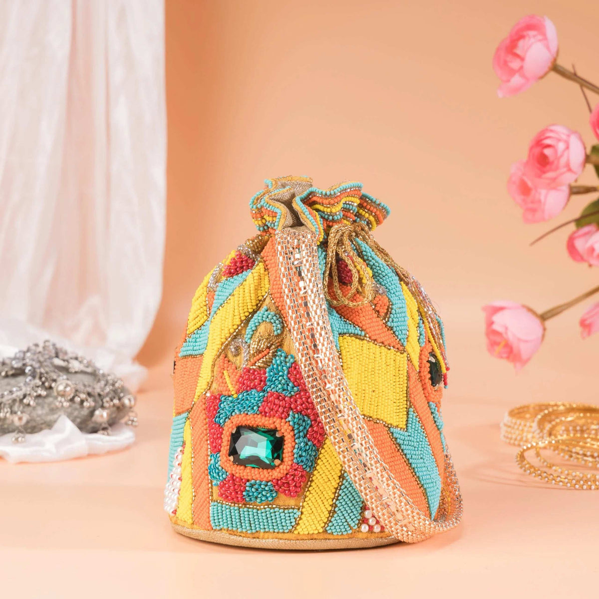 Chrome yellow beaded potli bag with a green stone, styled with pink blooms and bangles