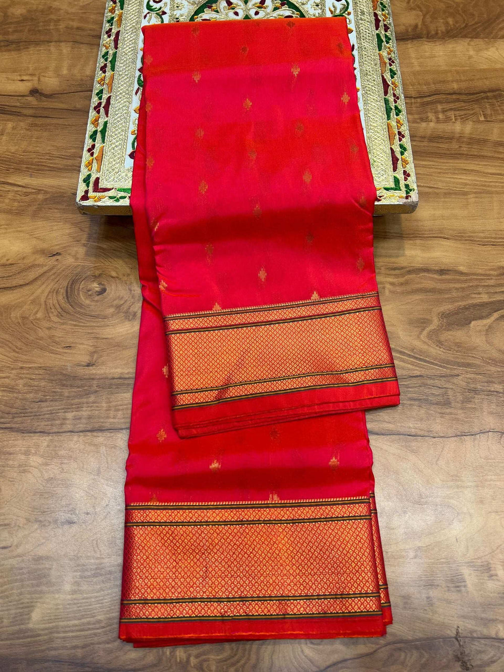 Coral red Kalanjali Paithani saree folded lengthwise, zari bootis across the body