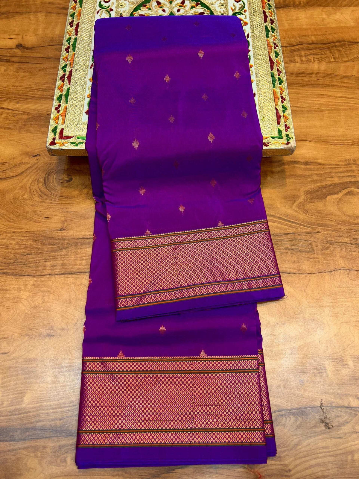 Violet Paithani saree folded on wood, gold bootis and red-gold woven border