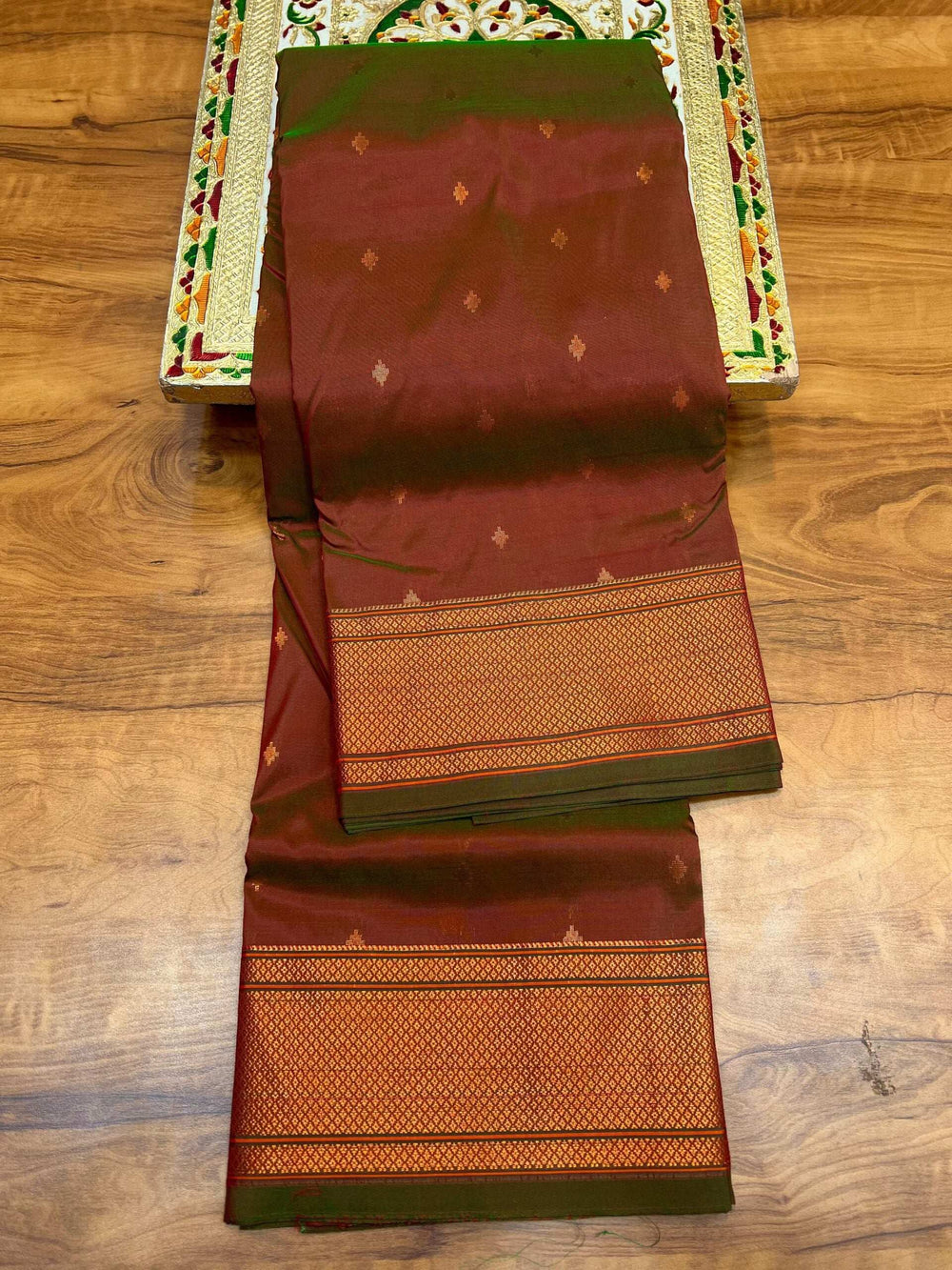 Rust brown Paithani saree with green edging, folded to show the woven border