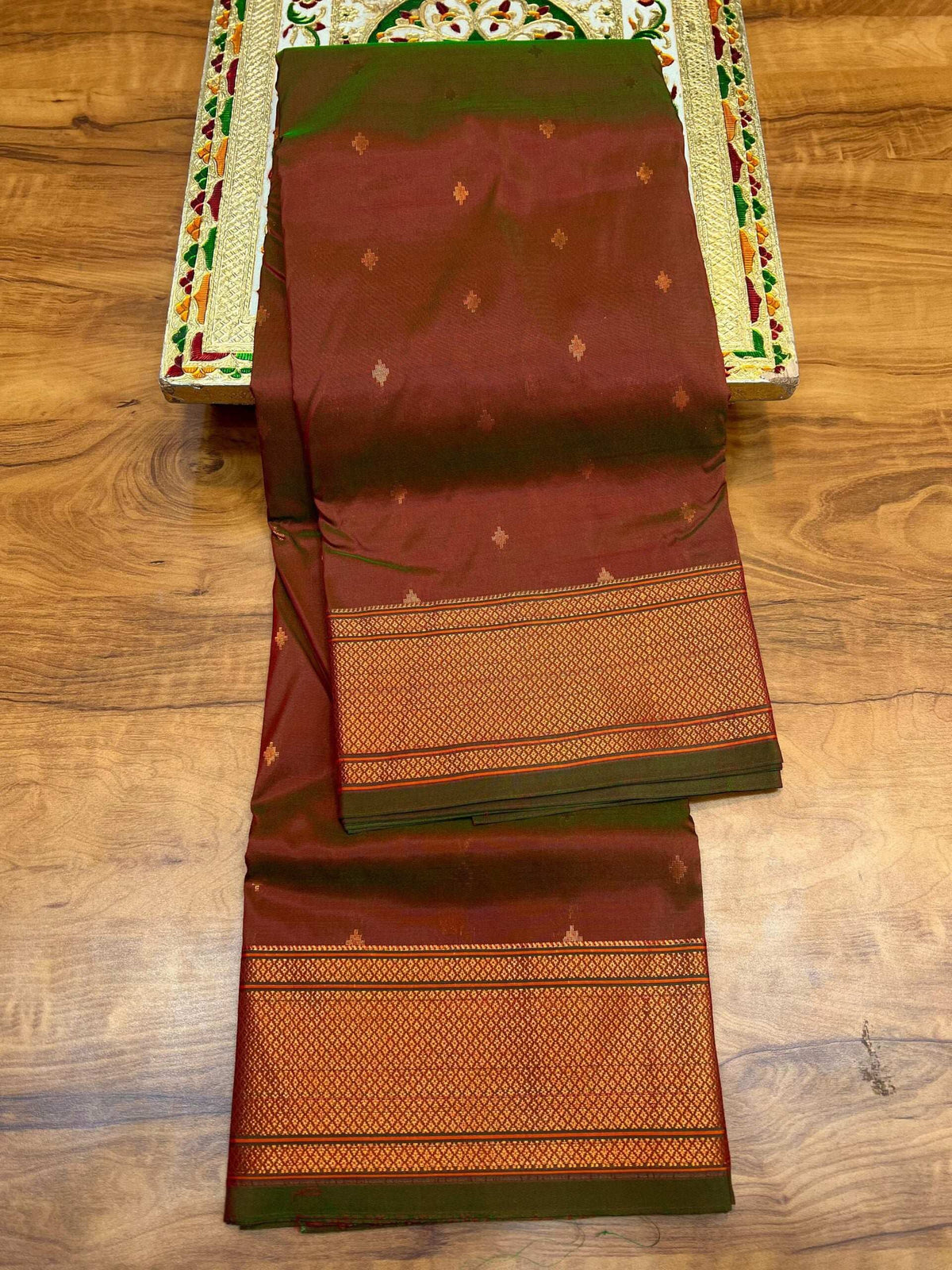 Rust brown Paithani saree with green edging, folded to show the woven border