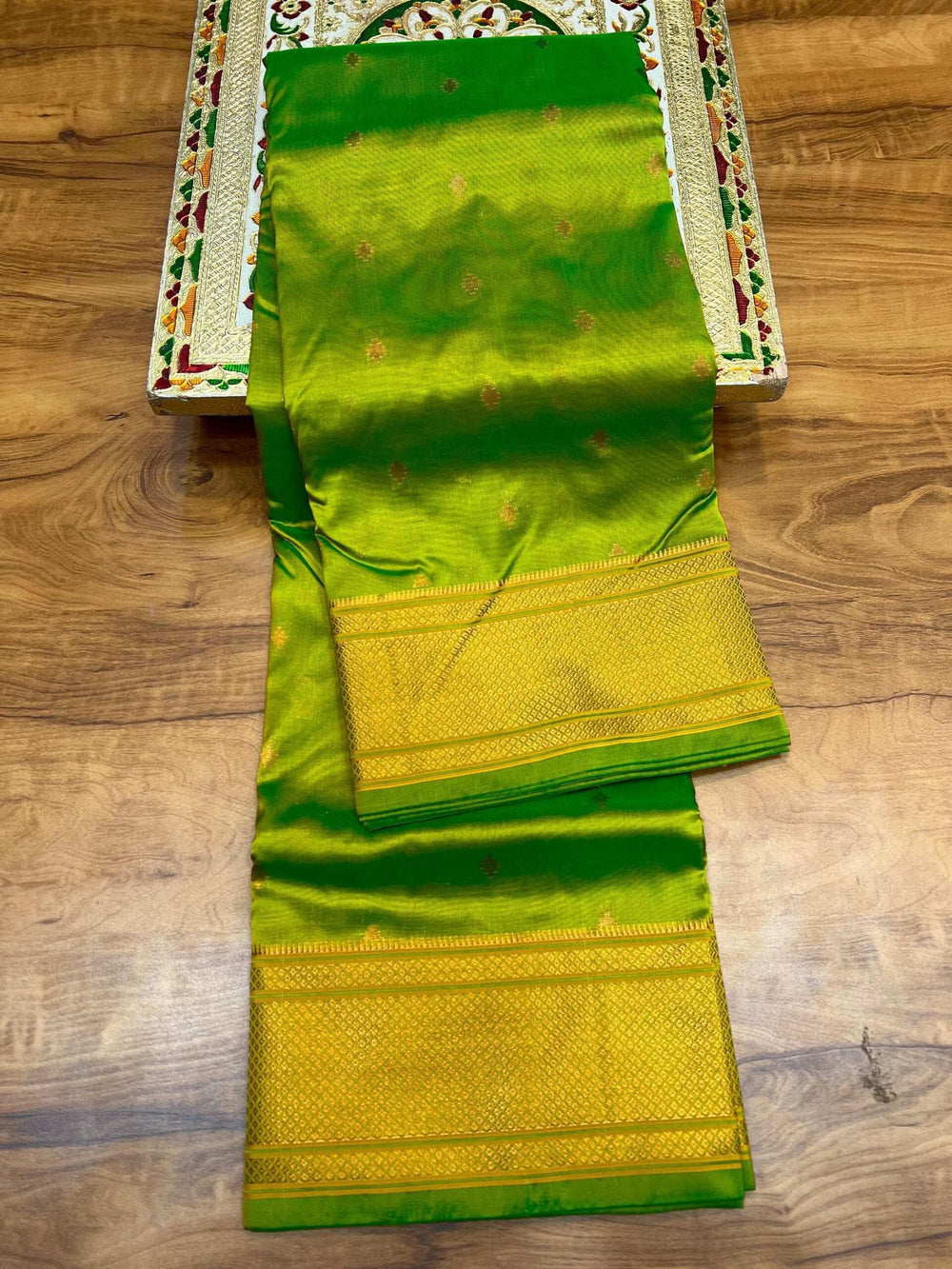 Parrot green saree folded lengthwise, broad gold zari border along the pallu
