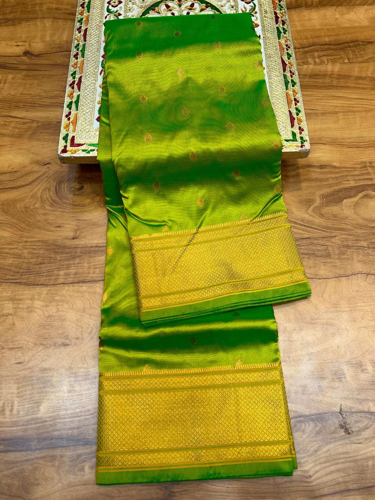 Parrot green saree folded lengthwise, broad gold zari border along the pallu