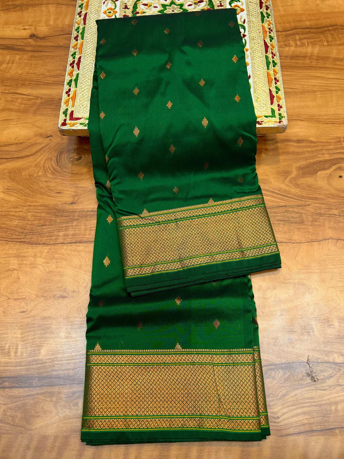 Dark green Paithani folded on a wooden floor, gold bootis dotting the body