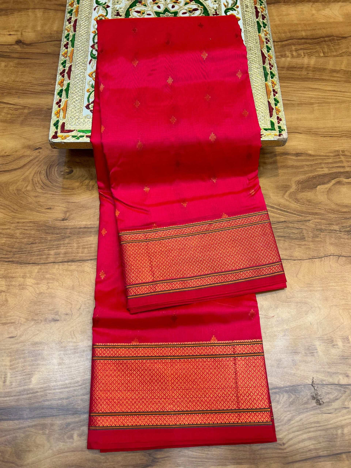 Red Paithani saree folded flat, zari bootis and orange-gold border stripes