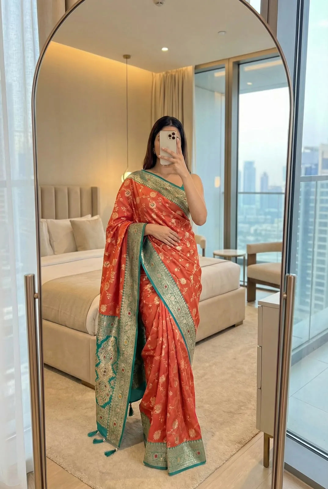 Coral orange soft silk saree with teal contrast border, draped with the pallu in front