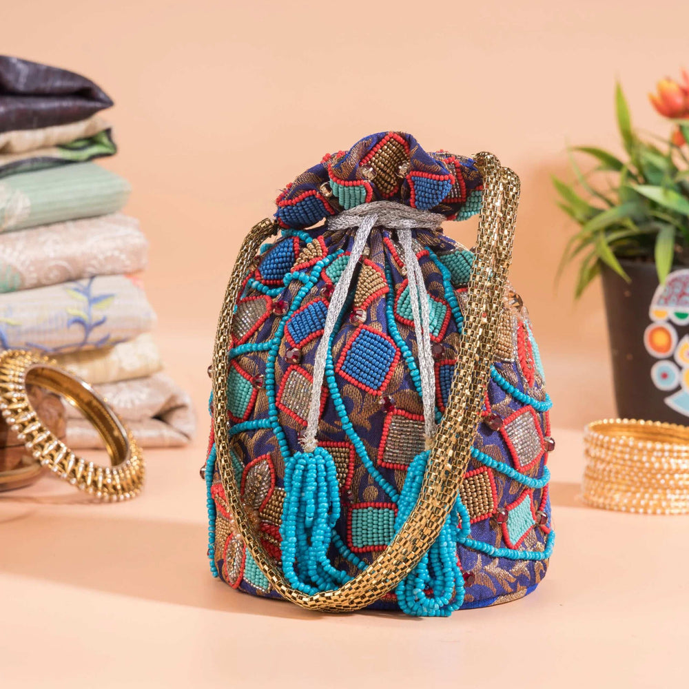 Blue beaded potli with geometric diamond motifs, styled beside bangles and folded fabrics