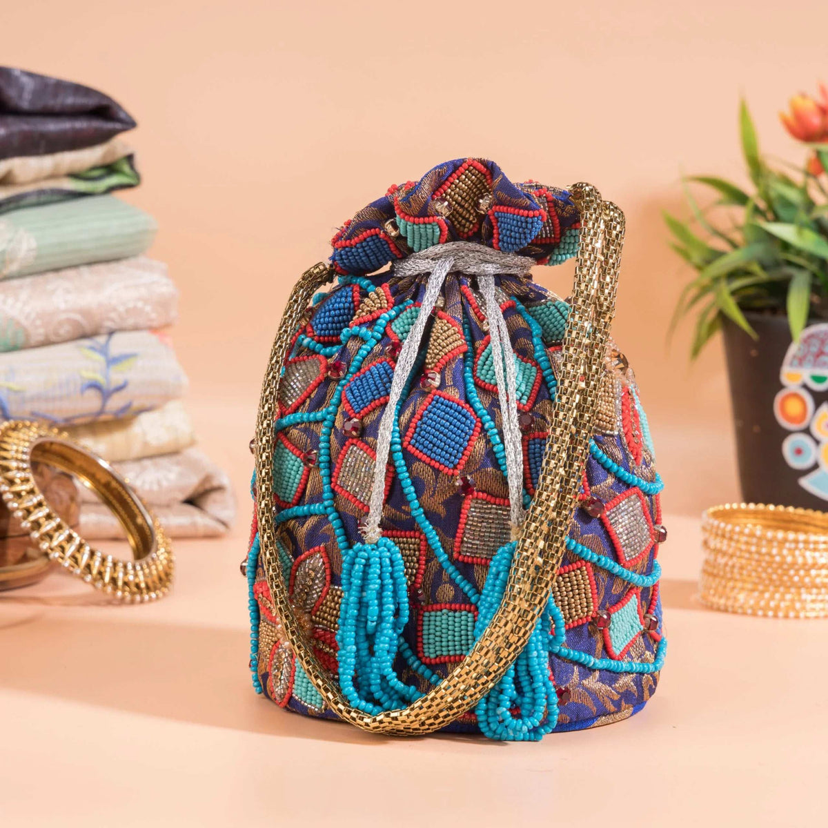 Blue beaded potli with geometric diamond motifs, styled beside bangles and folded fabrics