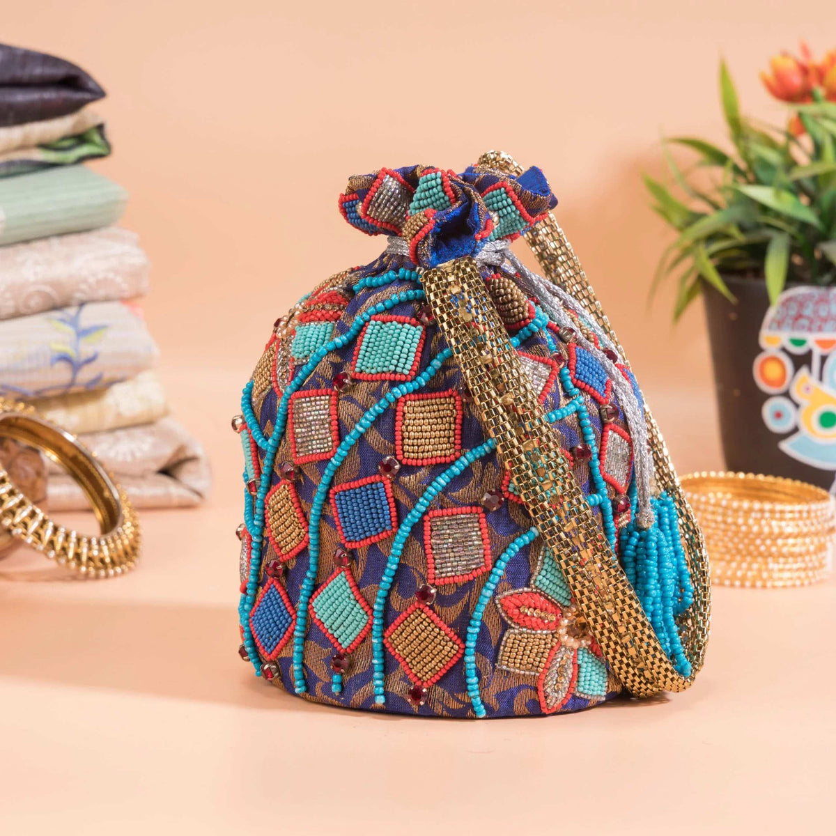Potli angled to show its braided gold handle and turquoise bead strands over blue beadwork