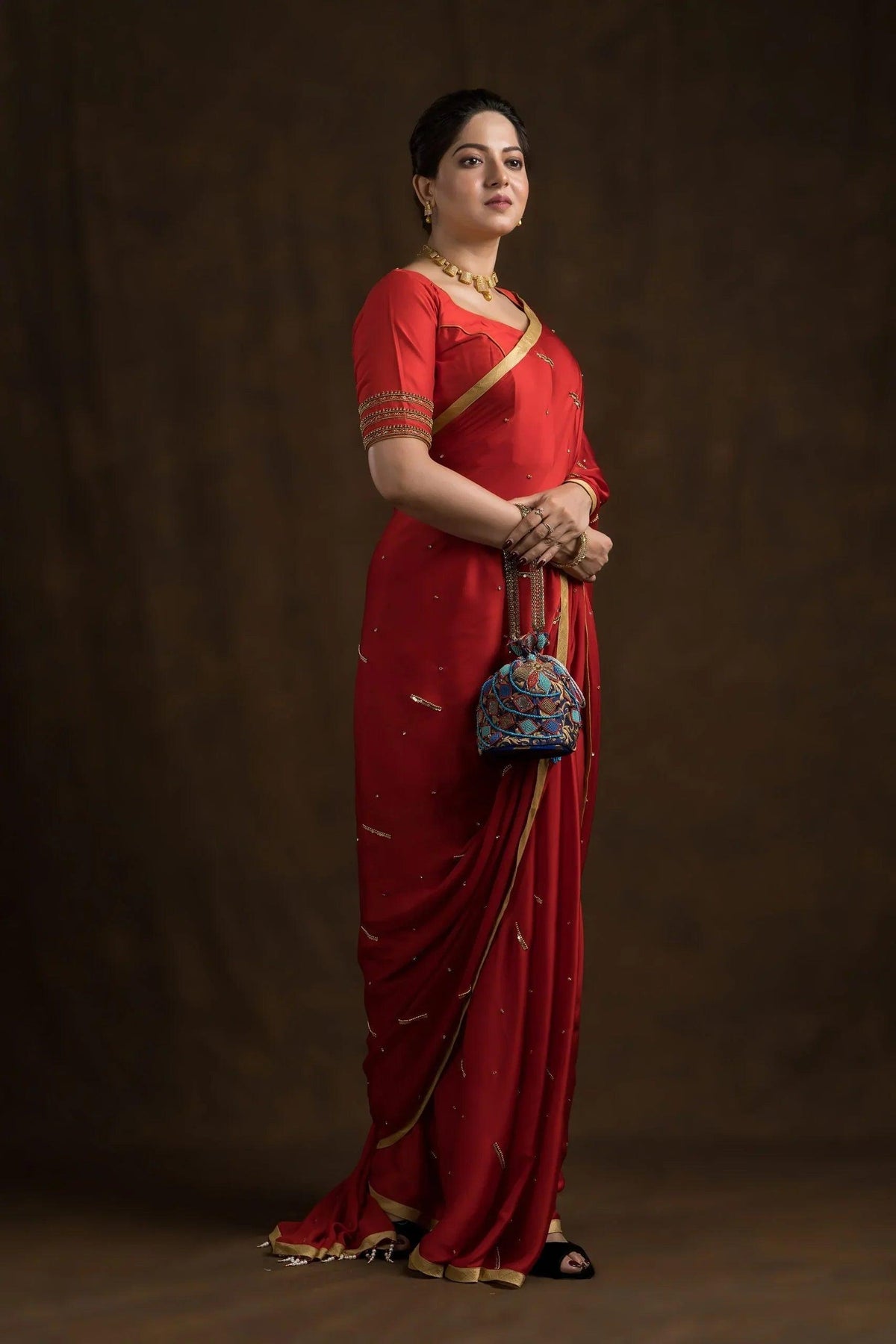 Model in a red saree holding the blue geometric potli at her side, full length
