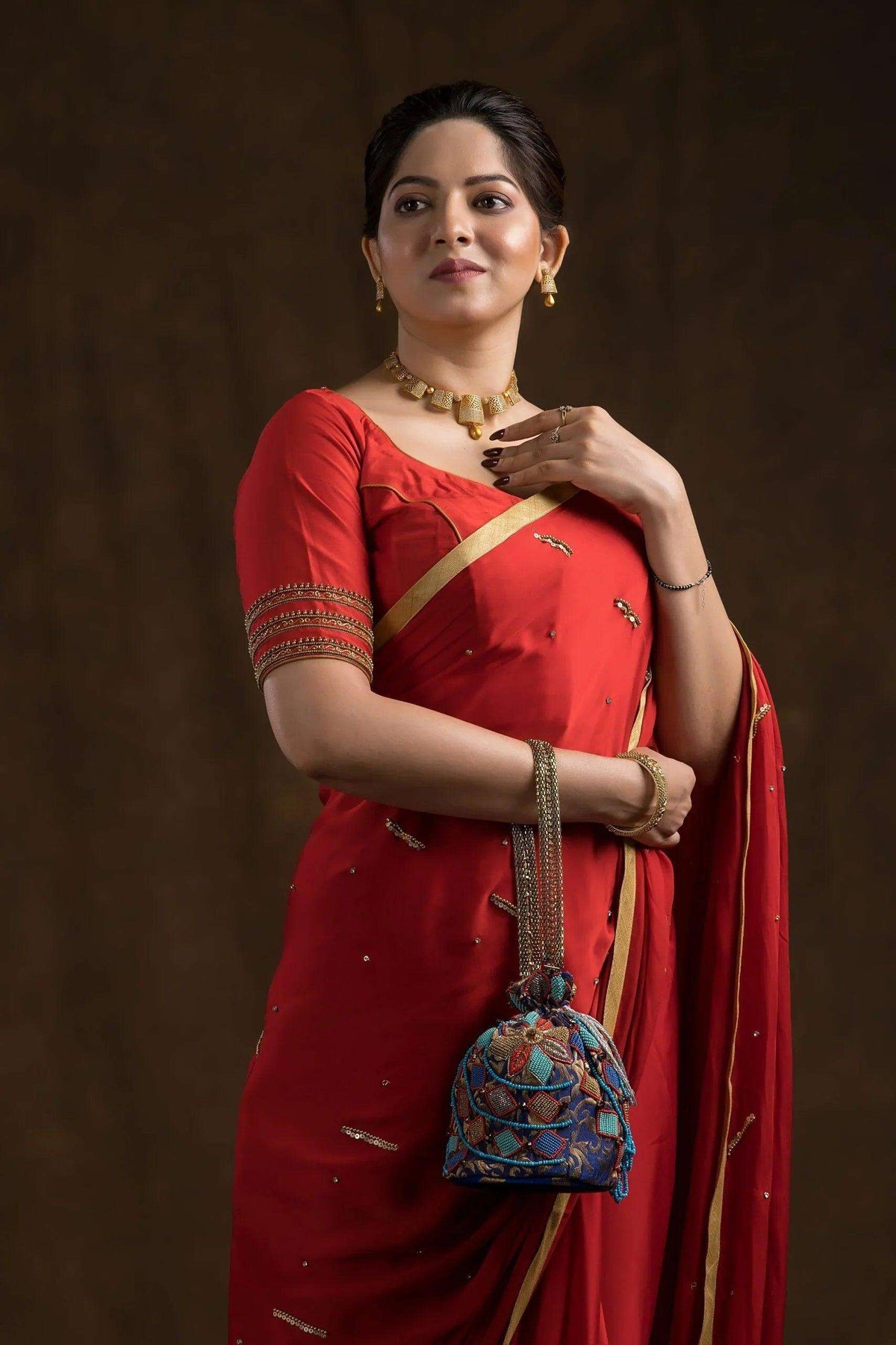 Blue potli bag held against a red saree, close enough to show the bead detail