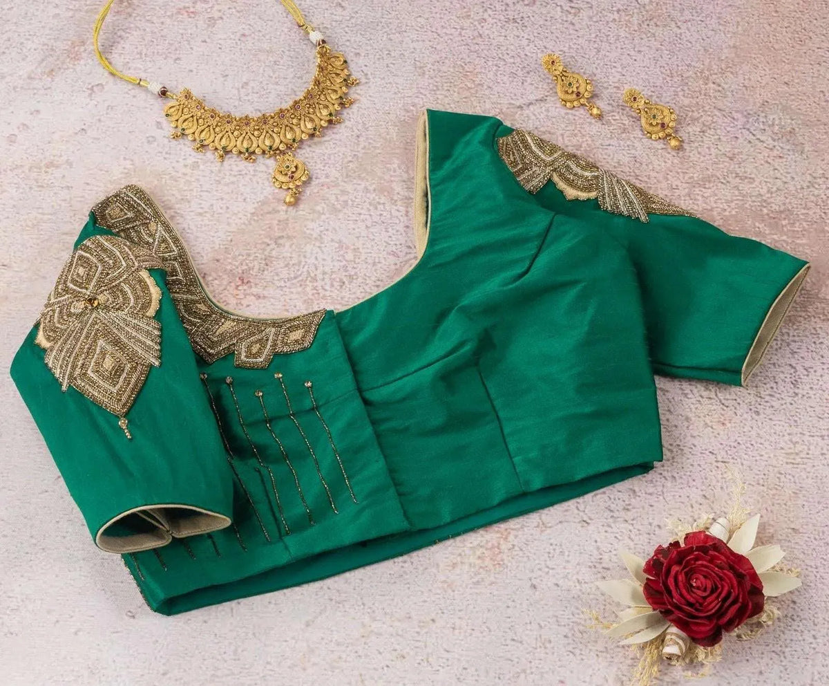 Angled flat-lay of the emerald blouse styled with gold jewellery and a rose