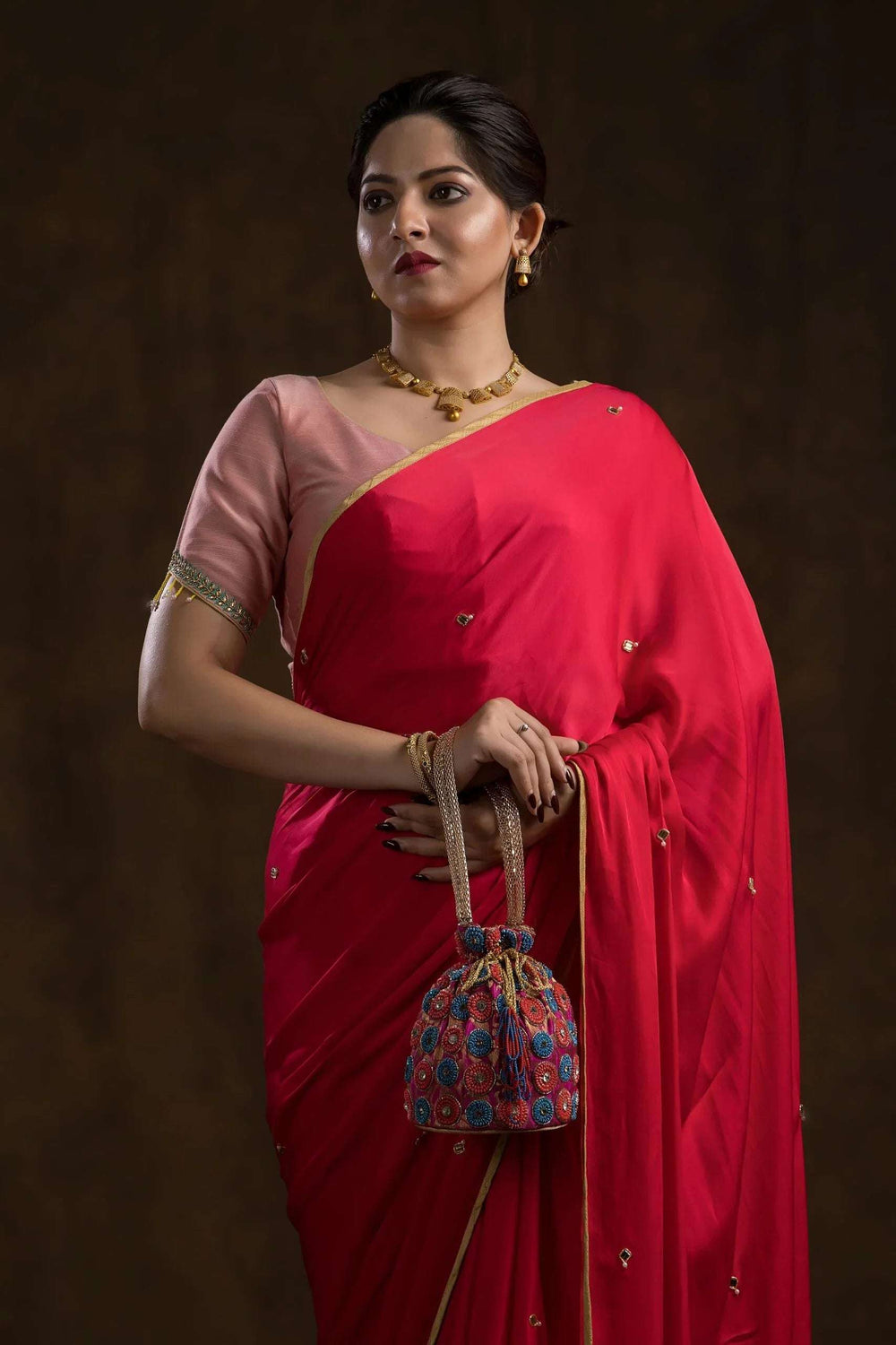 Model in a red saree holding the pink beaded potli bag by its gold cord