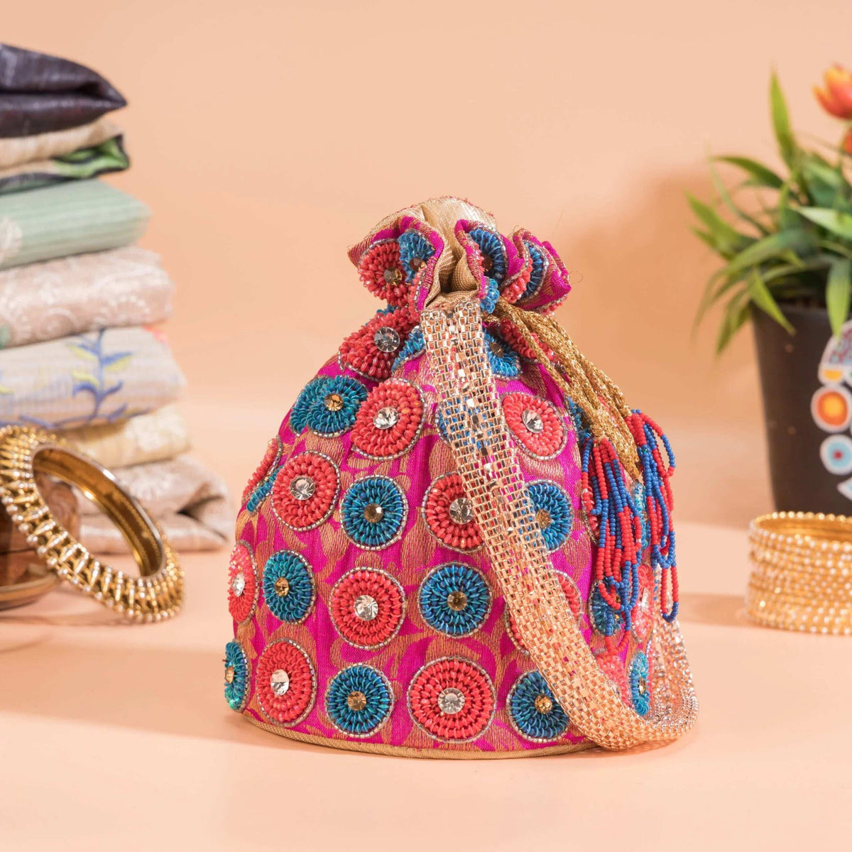 Pink potli with red and blue beaded spirals, styled with bangles and folded fabrics