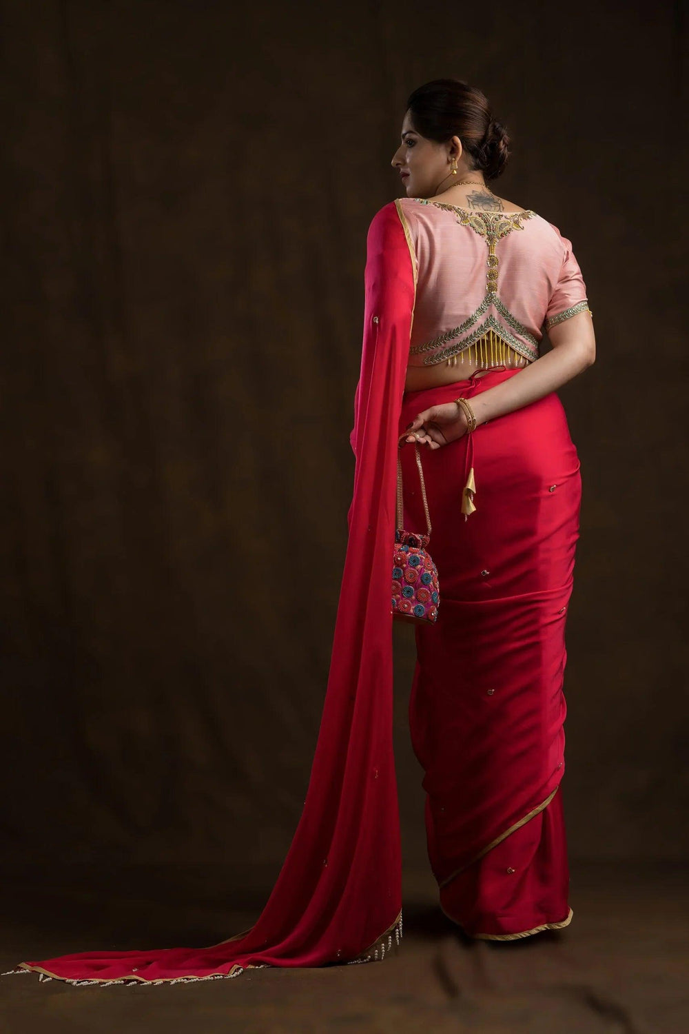 Full-length back view of a red saree drape, the small pink potli held at the waist