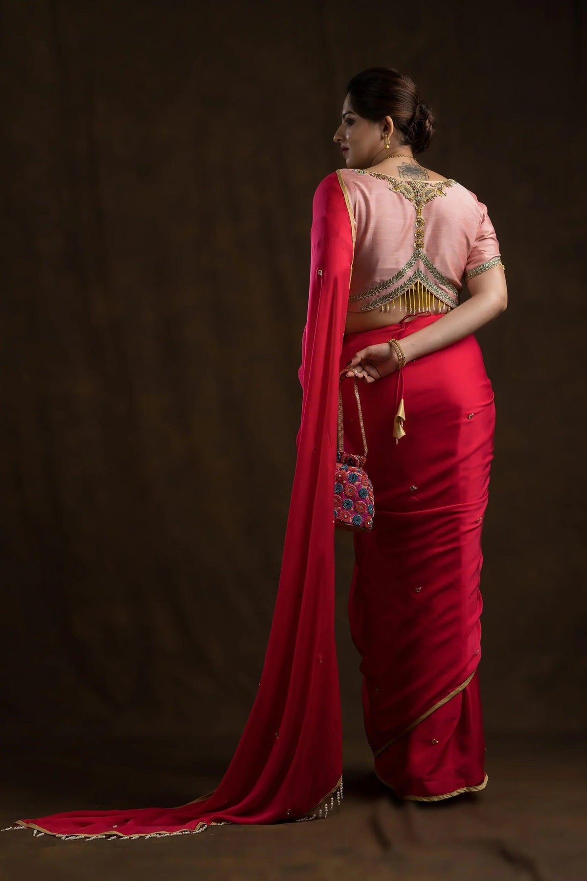 Full-length back view of a red saree drape, the small pink potli held at the waist