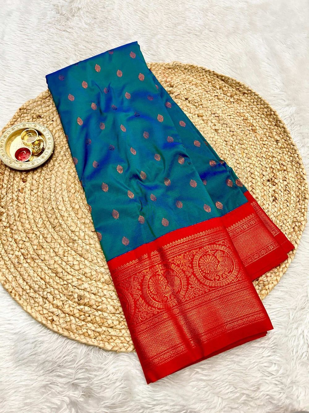 Teal blue saree with copper bootis and a red zari brocade border, flat lay