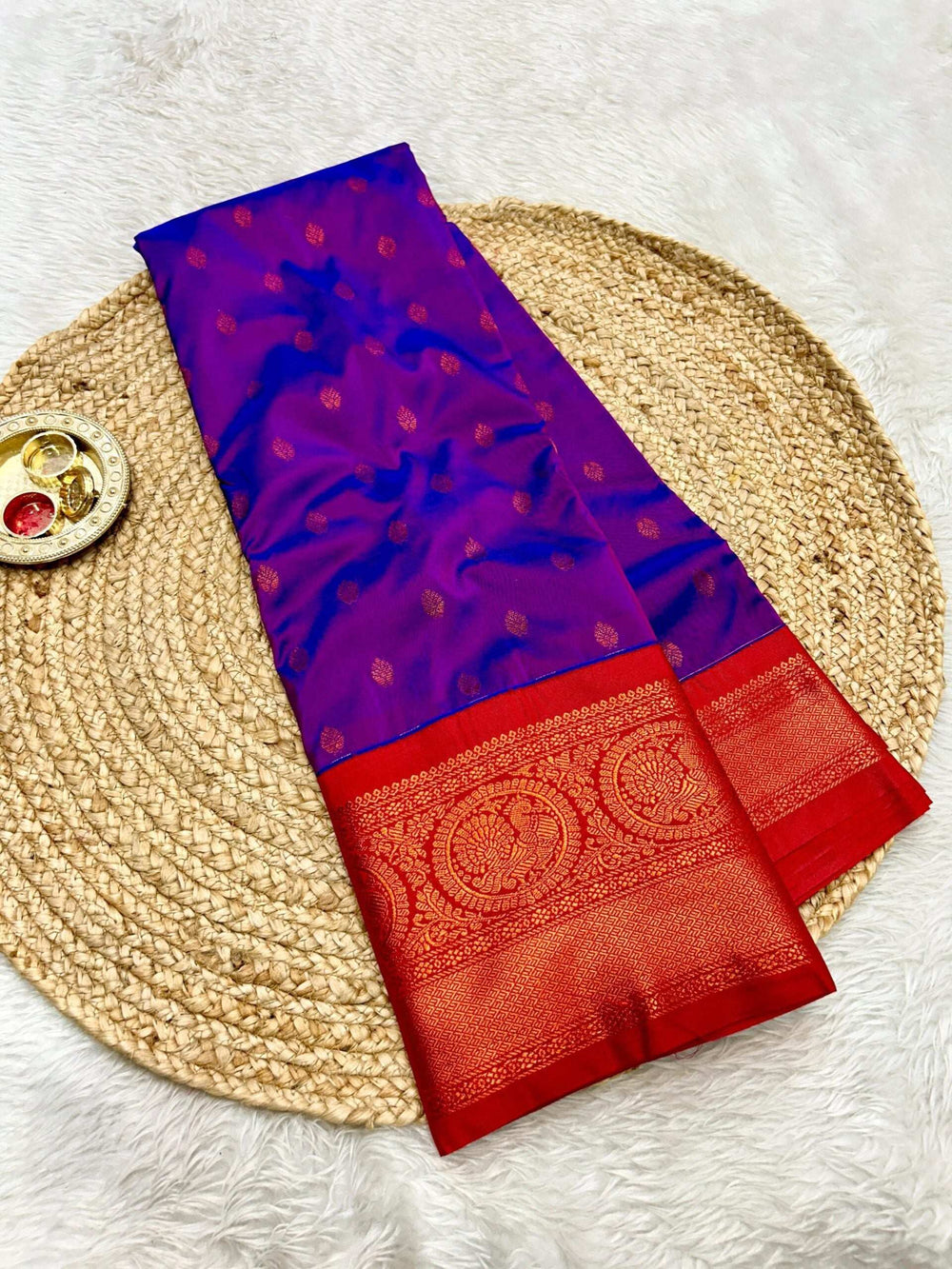 Purple-blue saree folded to show the wide red zari border and copper booti body