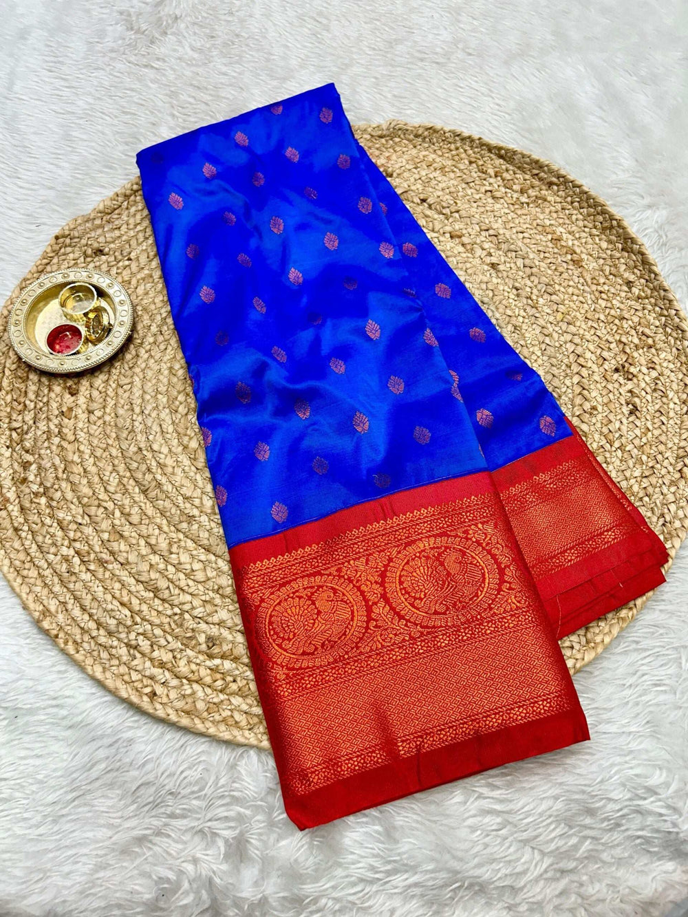 Bright blue saree folded on jute matting, red brocade border with peacock roundels