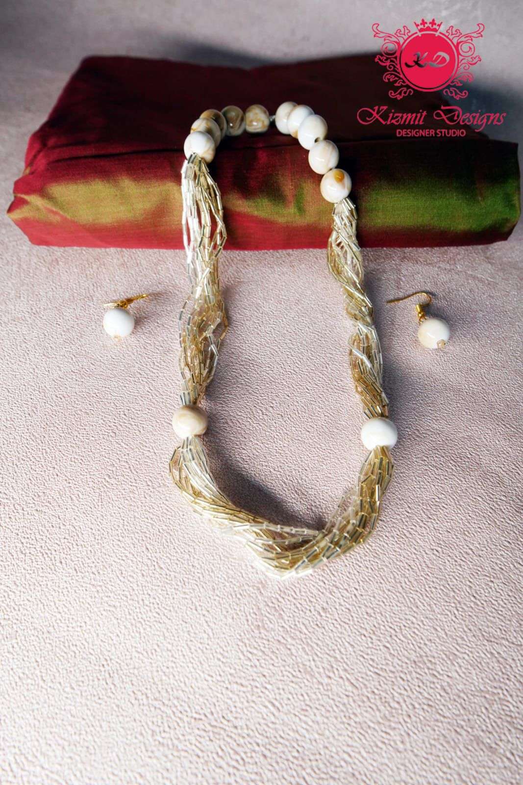 Multi-strand gold bead necklace with ivory beads laid flat beside matching earrings