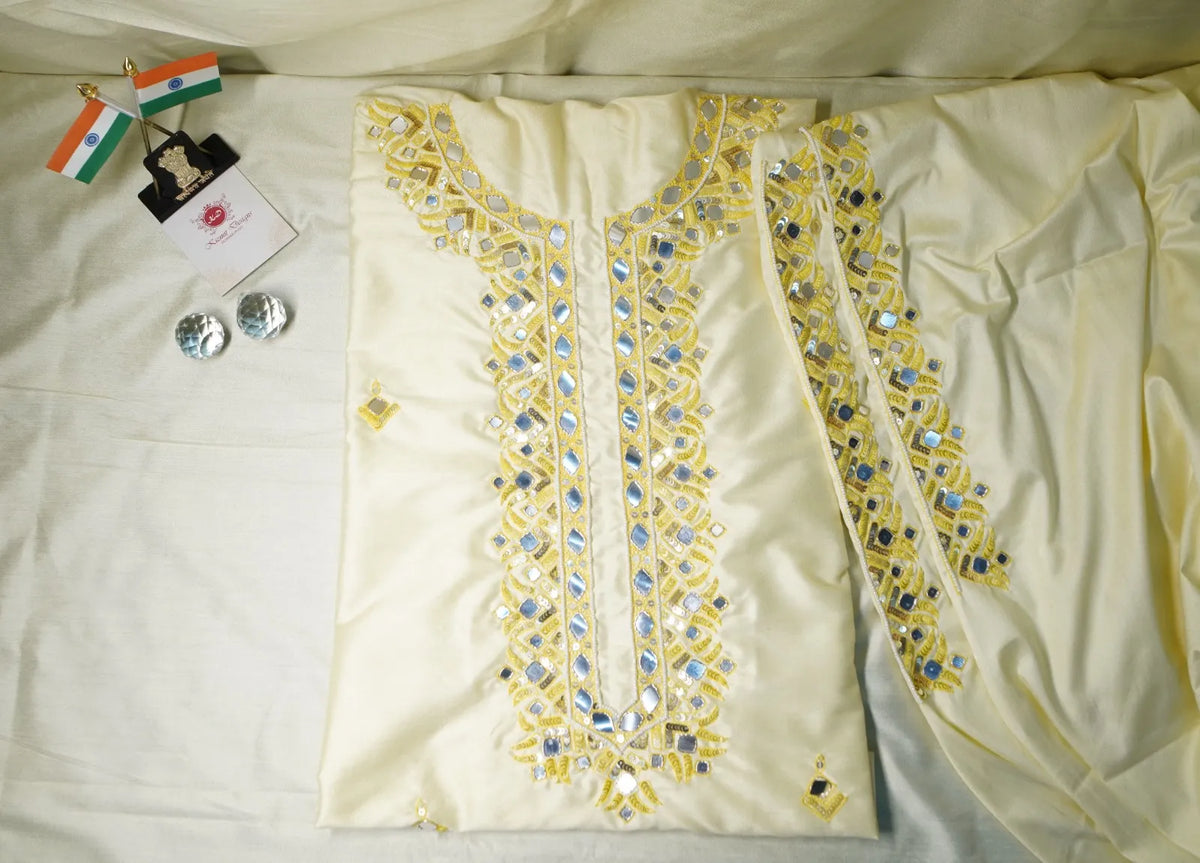 Unstitched pale yellow fabric set laid out with mirror-work embroidery at the neckline