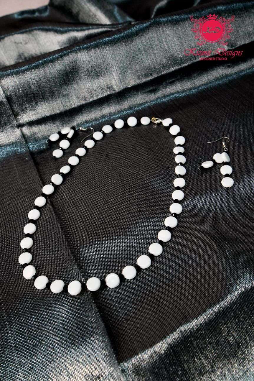 White beaded necklace and earrings laid flat on dark grey fabric