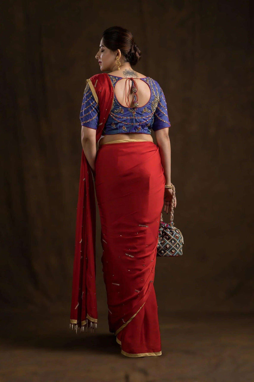 Full length back view, red saree drape with the embroidered blouse and a potli bag in hand