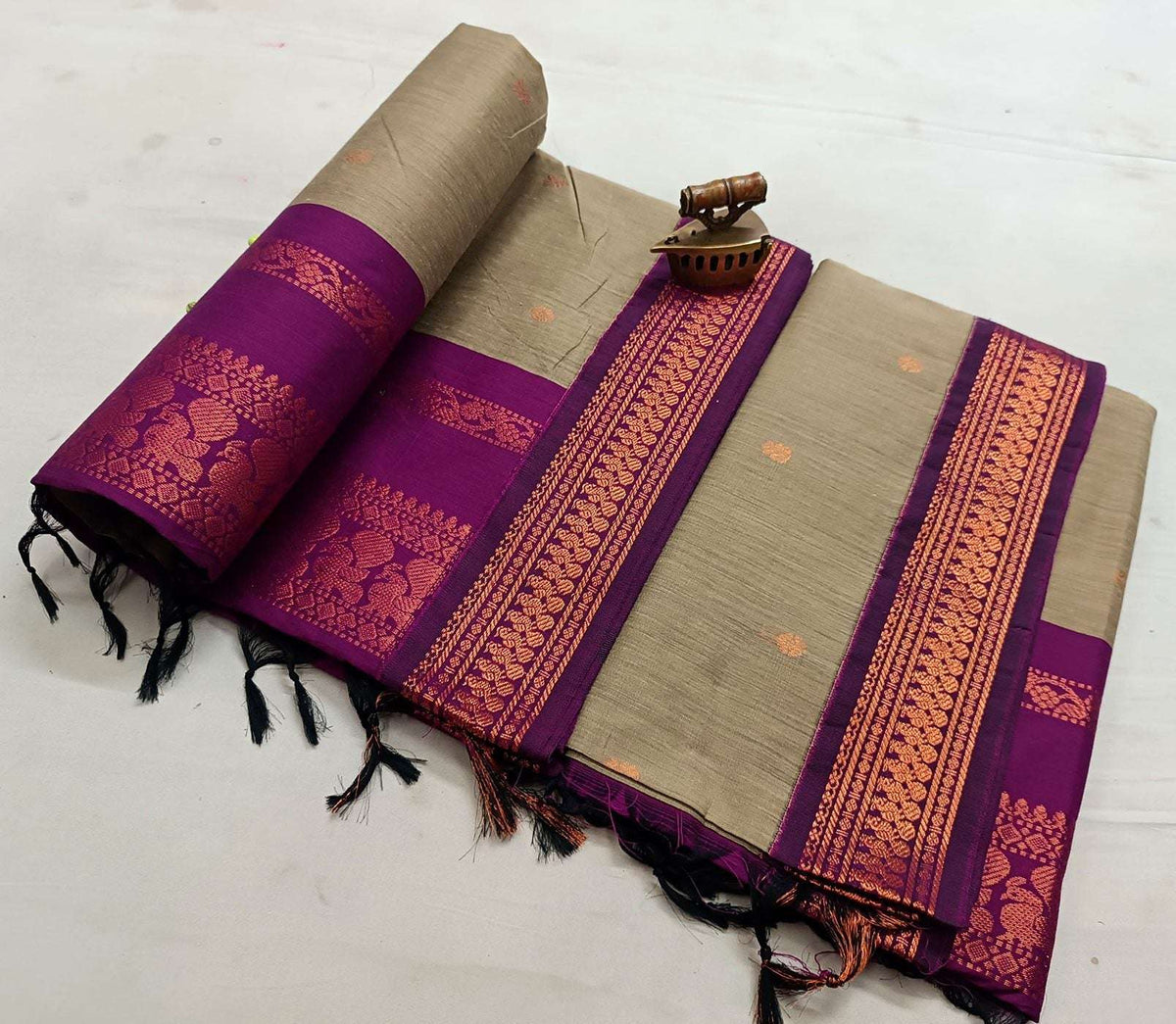 Beige saree body with a purple zari border and copper bootis, folded flat