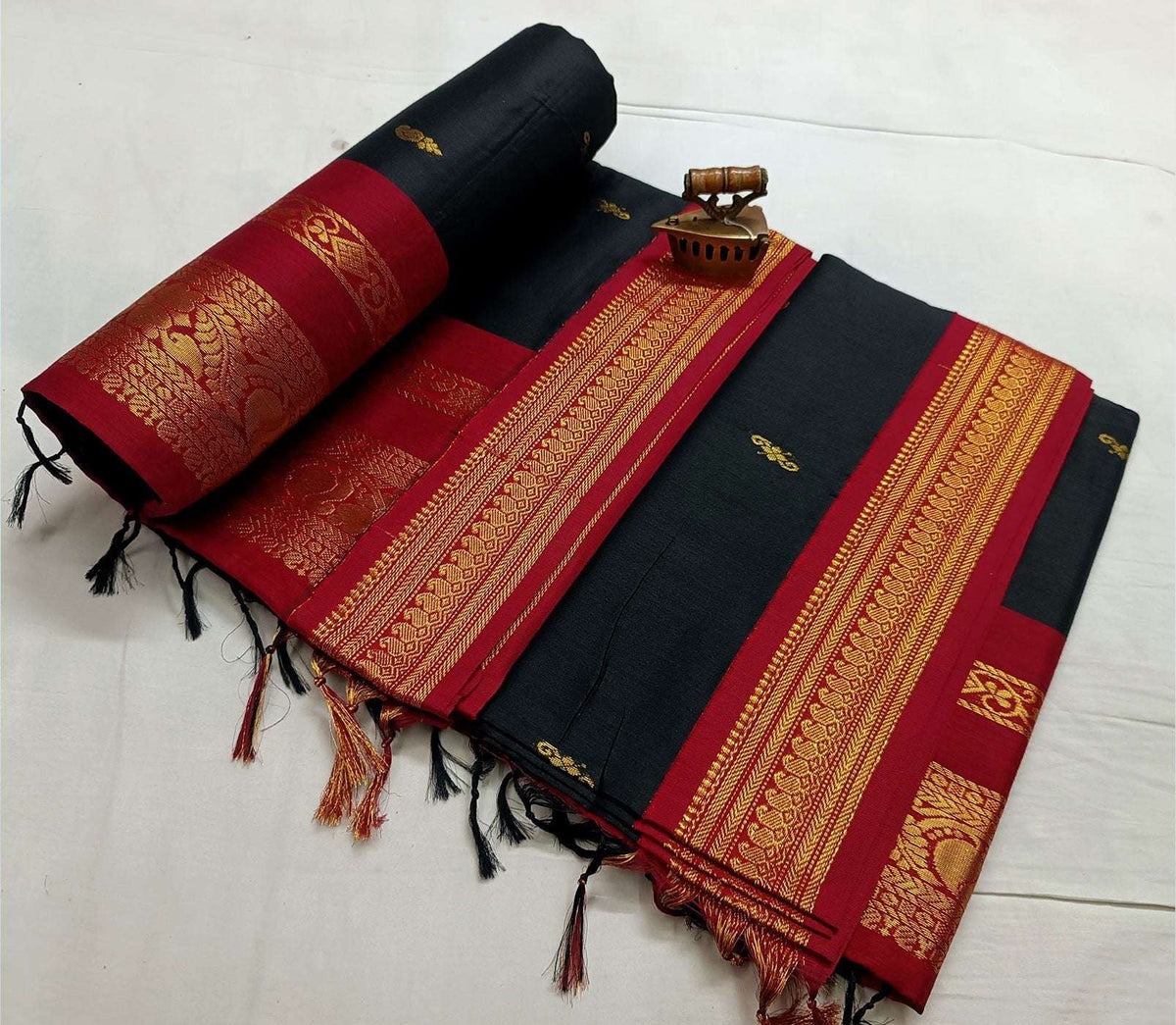Black body with red korvai border, gold zari stripes and knotted pallu tassels