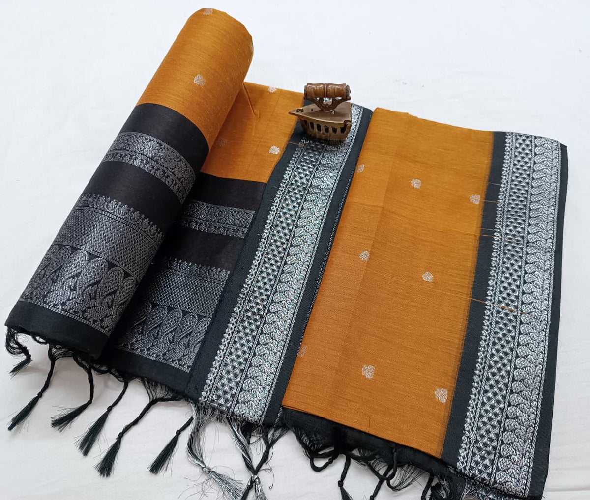 Mustard body with black border worked in silver zari, pallu rolled up at the left