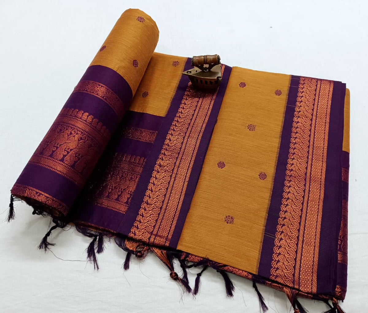 Mustard saree with a wide purple border in copper zari, rolled pallu showing figure motifs